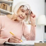 Elderly woman writing in a notebook while adjusting her glasses