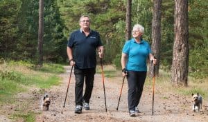 Older couple with walking poles enjoying an outdoor hike with their two dogs.