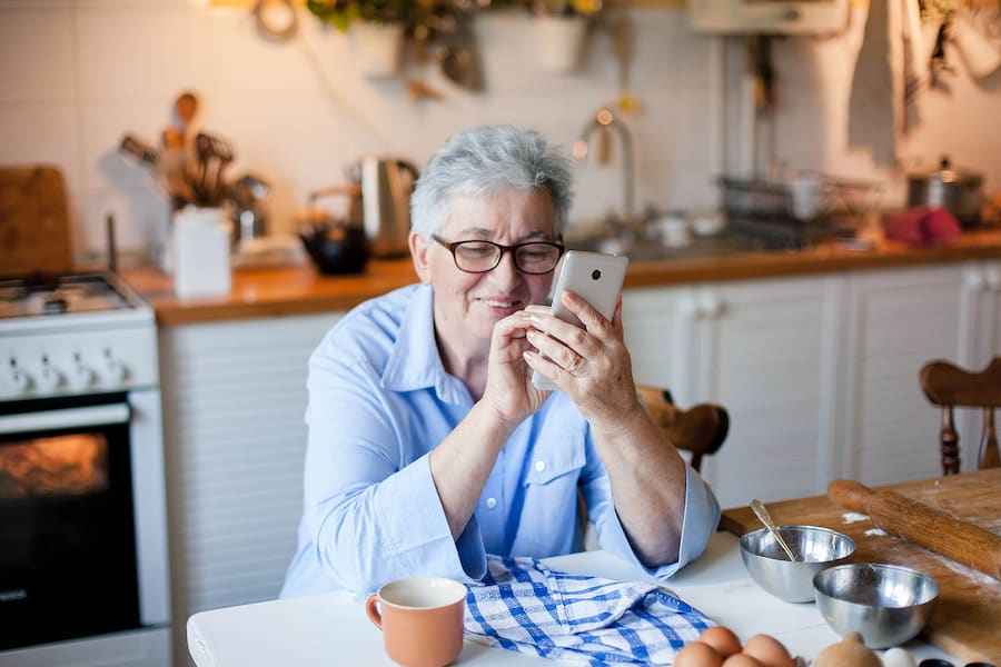 An older woman safely video chatting with loved ones before she begins to cook.