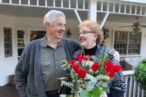 Smiling elderly couple holding a bouquet of red roses on a porch