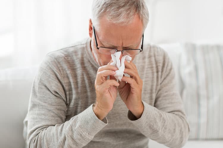 An older man who is blowing his nose due to suffering from the flu.