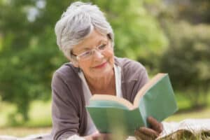 Senior woman with gray hair reading a book outdoors on a sunny day