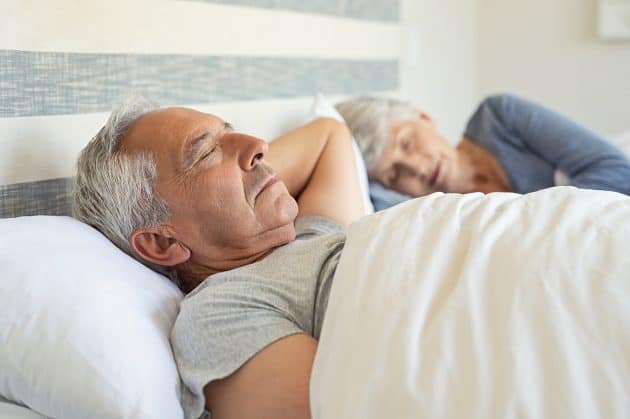 A senior man and woman sleeping in their bed in the morning.