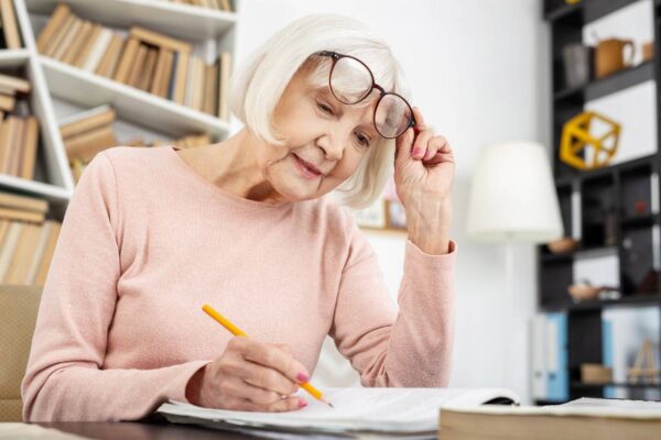 Elderly woman writing in a notebook while adjusting her glasses