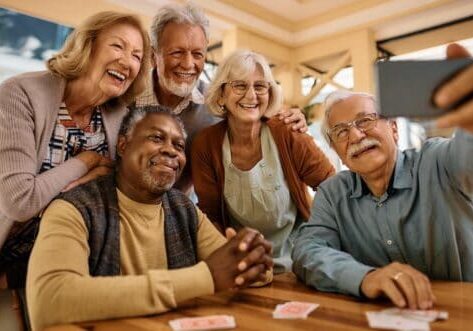 Multiracial group of happy senior people taking selfie with cell phone in nursing home.