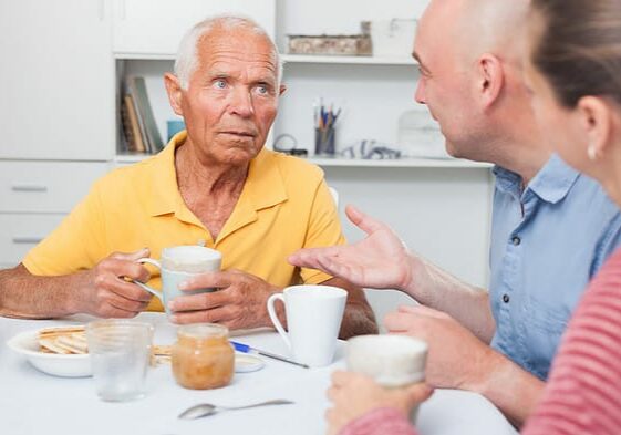 Portrait of mature man with daughter and friend talking at table with cup of tea