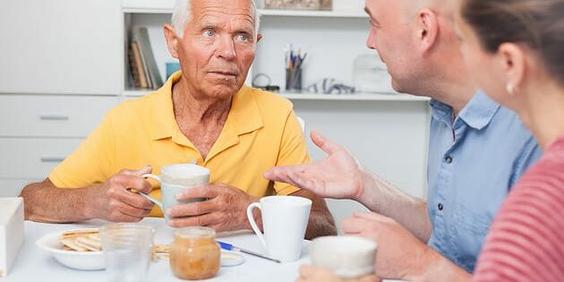 Portrait of mature man with daughter and friend talking at table with cup of tea