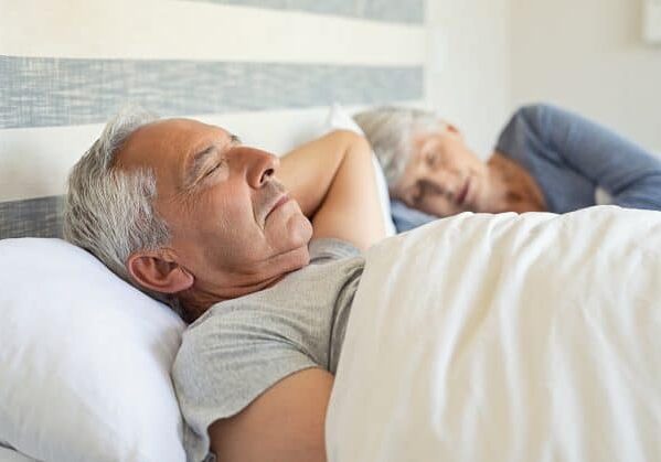 A senior man and woman sleeping in their bed in the morning.