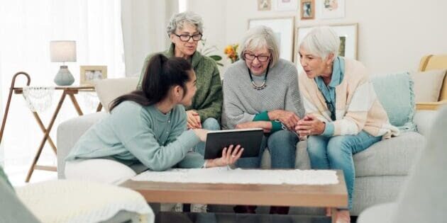 Tablet, friends and senior women on sofa online for social media, streaming movies and internet search. Retirement home, social reunion and caregiver on digital tech for learning, teaching and help