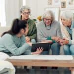 Tablet, friends and senior women on sofa online for social media, streaming movies and internet search. Retirement home, social reunion and caregiver on digital tech for learning, teaching and help
