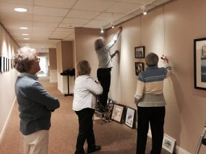 Members of the Dexter Painter's hang the show in Gallery 100 with help from Gallery 100 resident coordinator Lois deLeon.